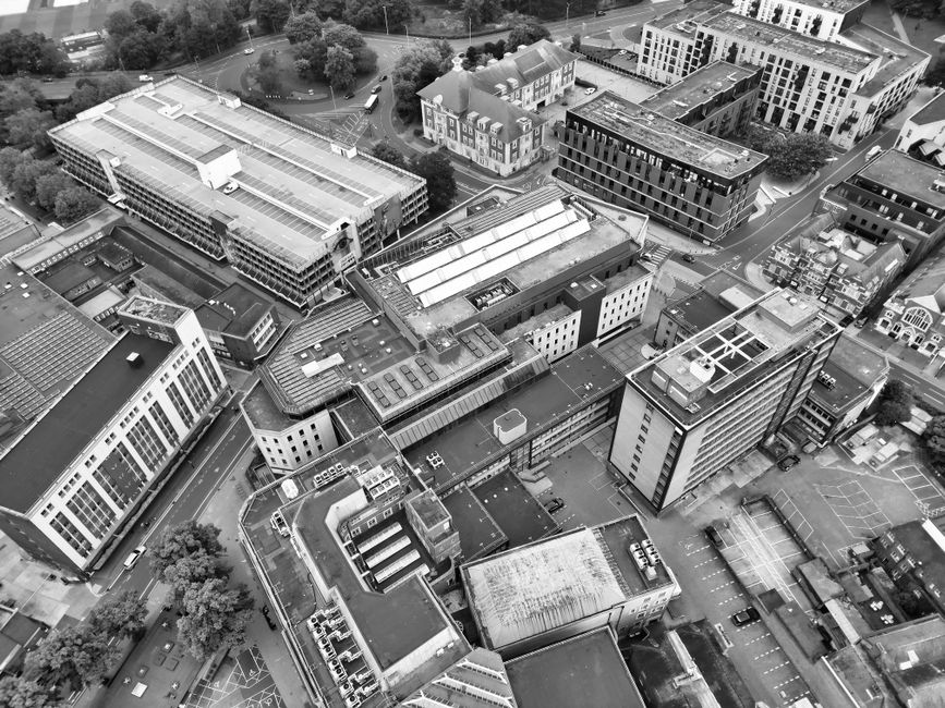 An aerial black-and-white photograph shows a dense urban area with multiple modern office buildings and commercial structures. The buildings vary in size, shape, and architectural style, featuring fla
